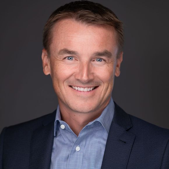 Smiling man in a navy blazer and blue shirt against a dark gray background