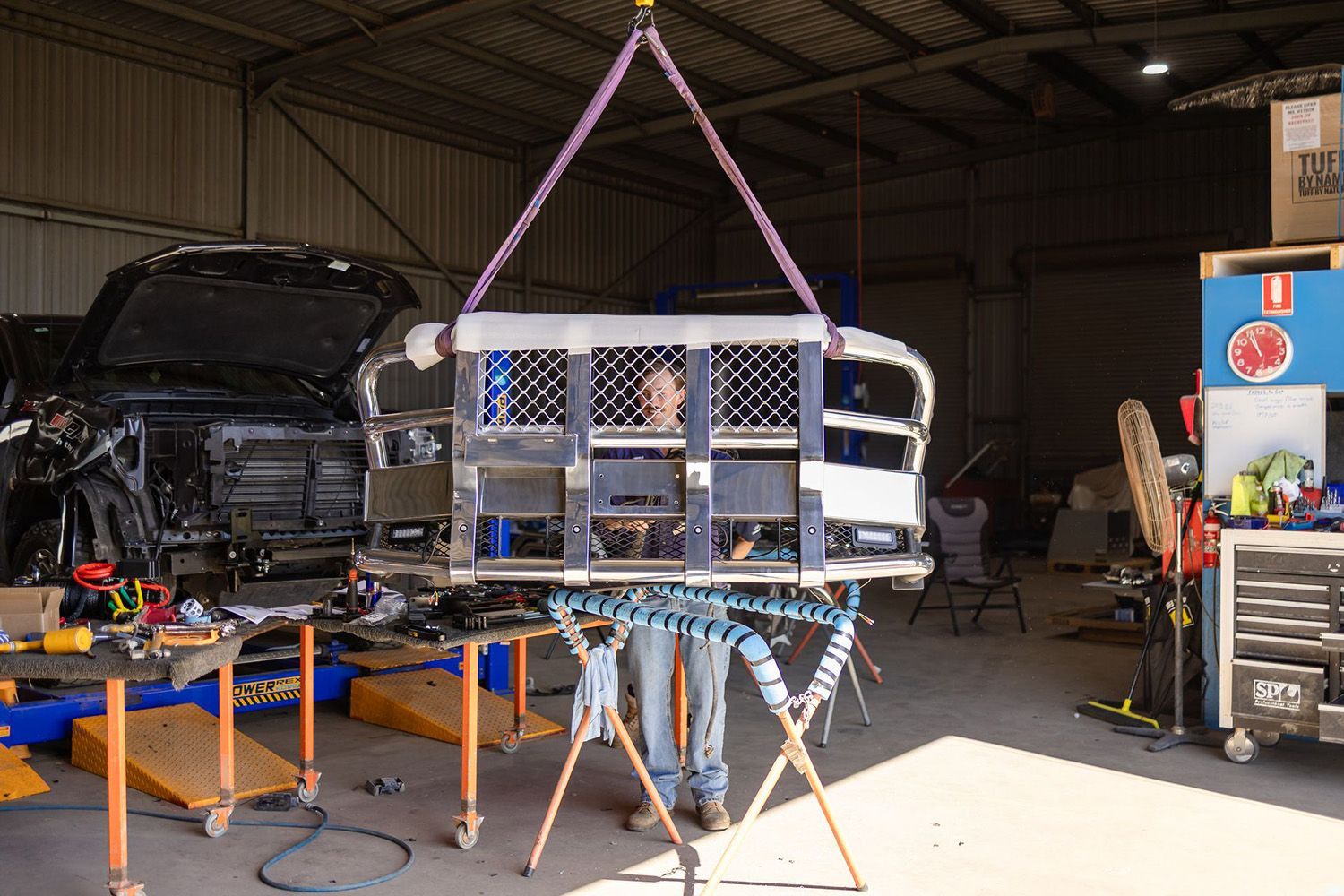 A Person Stands Beneath A Lifted Truck Bed In A Workshop
