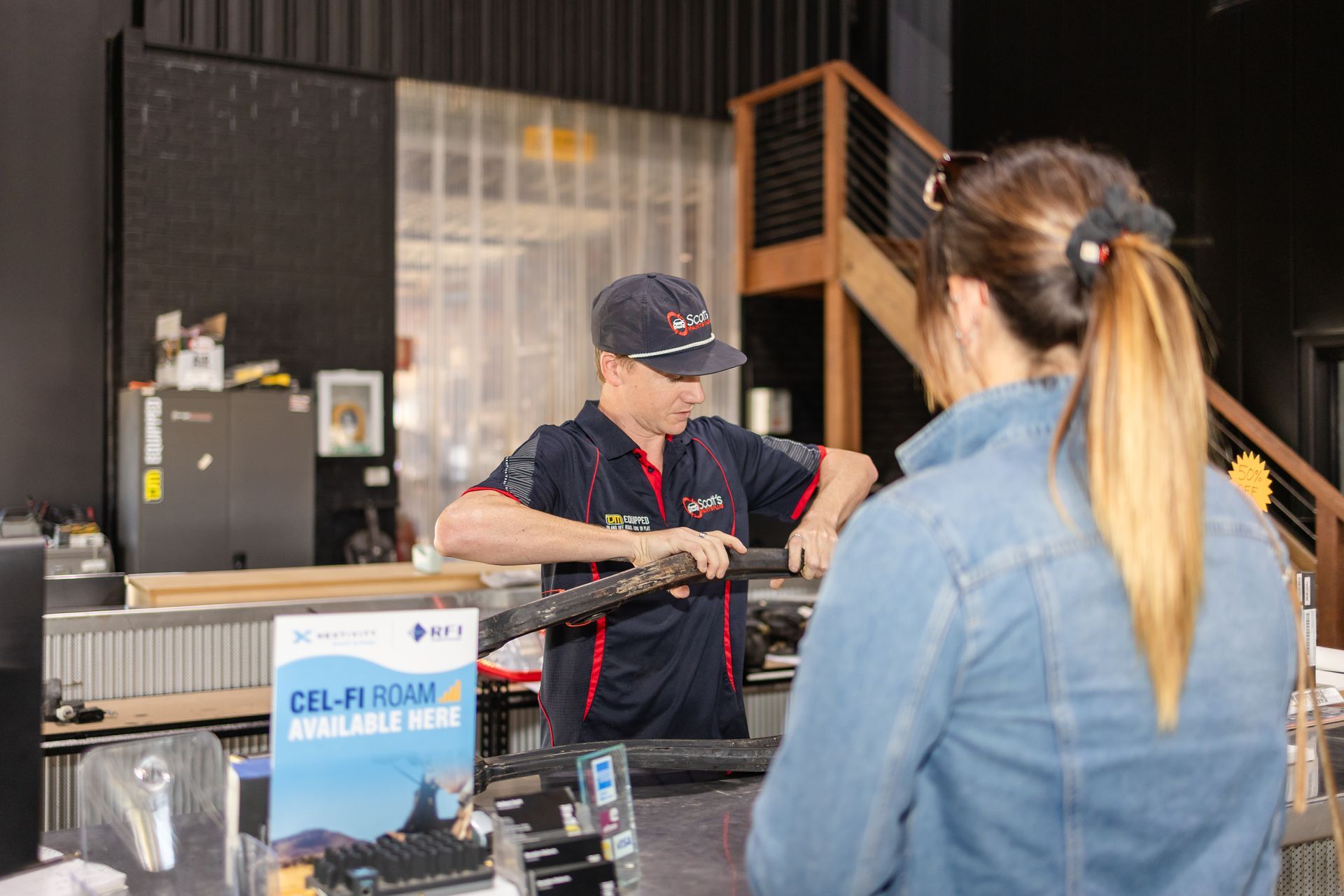 A man in blue behind the counter helping a woman — Scott's 4WD Parts Plus In Dubbo, NSW