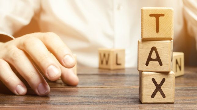 Stacked wooden blocks spelling TAX on a desk beside a hand