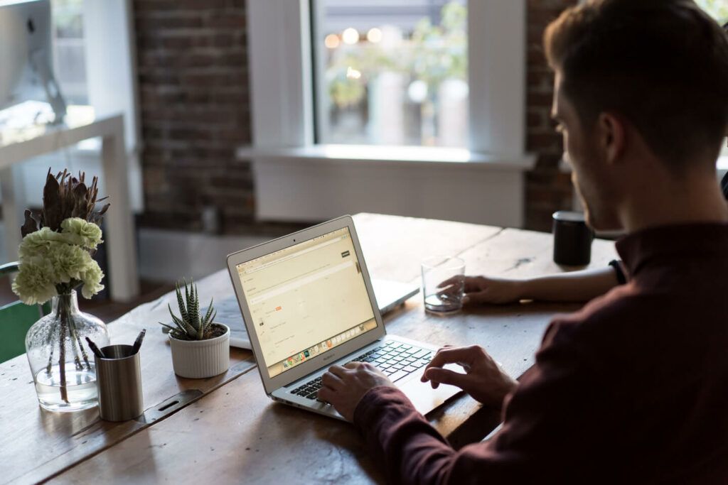 Person working on a laptop at a wooden desk in a bright home office