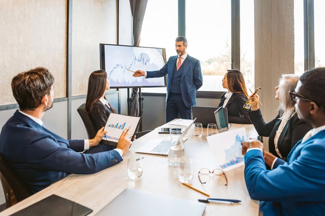 Business presentation in a conference room, with a presenter gesturing beside a slide screen as colleagues watch