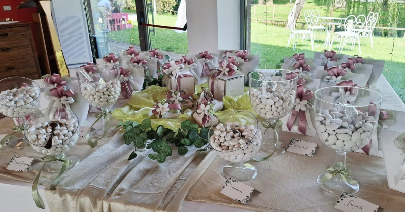 Un tavolo da banchetto decorato con centrotavola floreali, bicchieri e nastri rosa in una stanza luminosa.