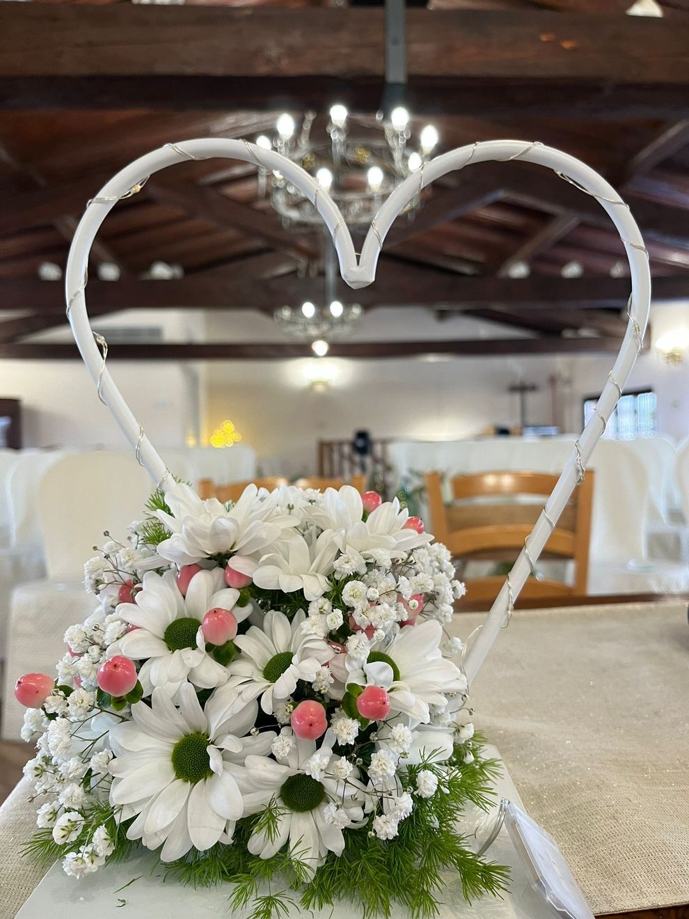 Elegante tavolo da banchetto con centrotavola floreali dai colori pastello, tovaglioli rosa e bicchieri in una stanza luminosa.