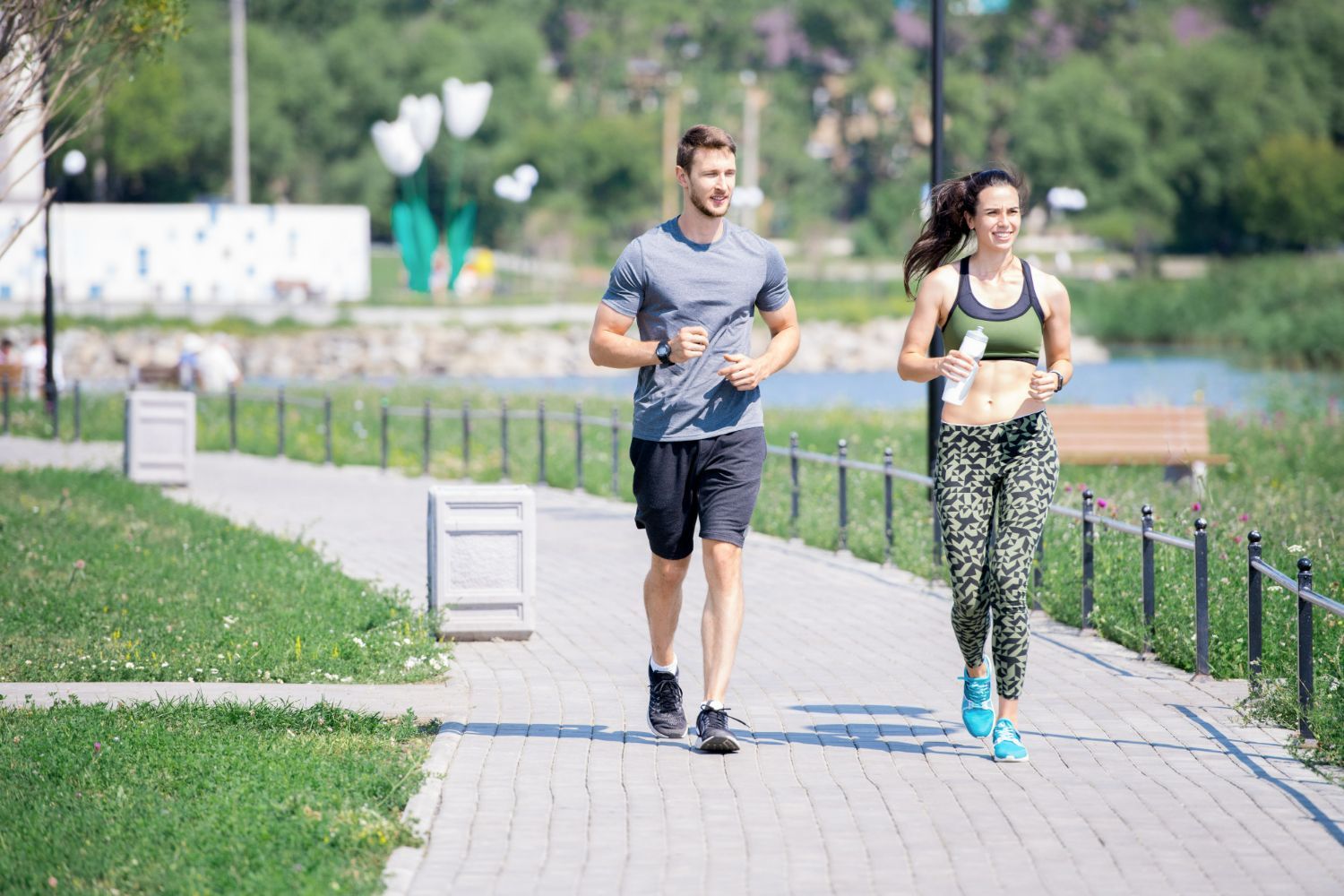 A man and woman running together on a paved path in a park, smiling.