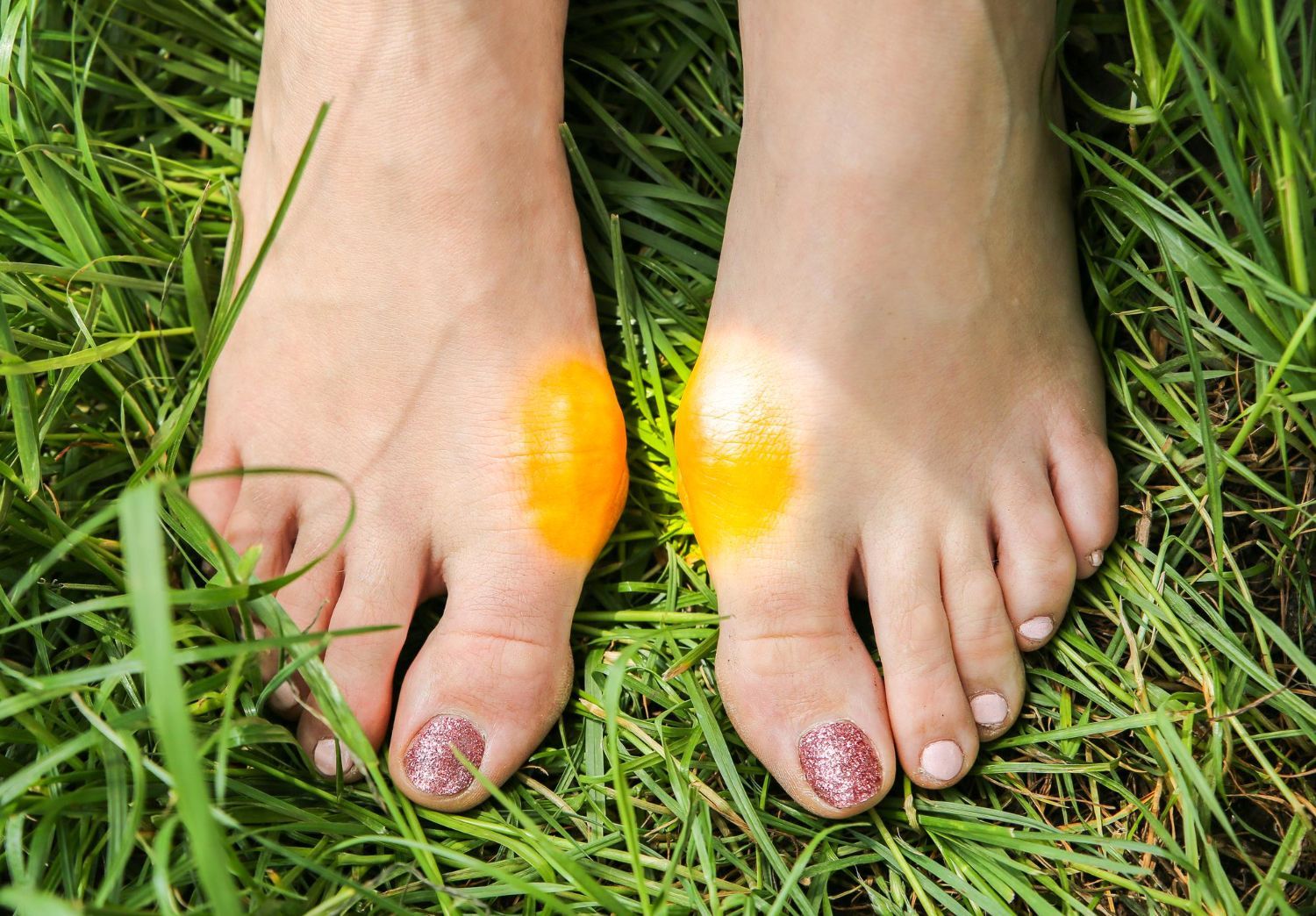 Bare feet on grass with bright orange and yellow paint on the tops of both feet
