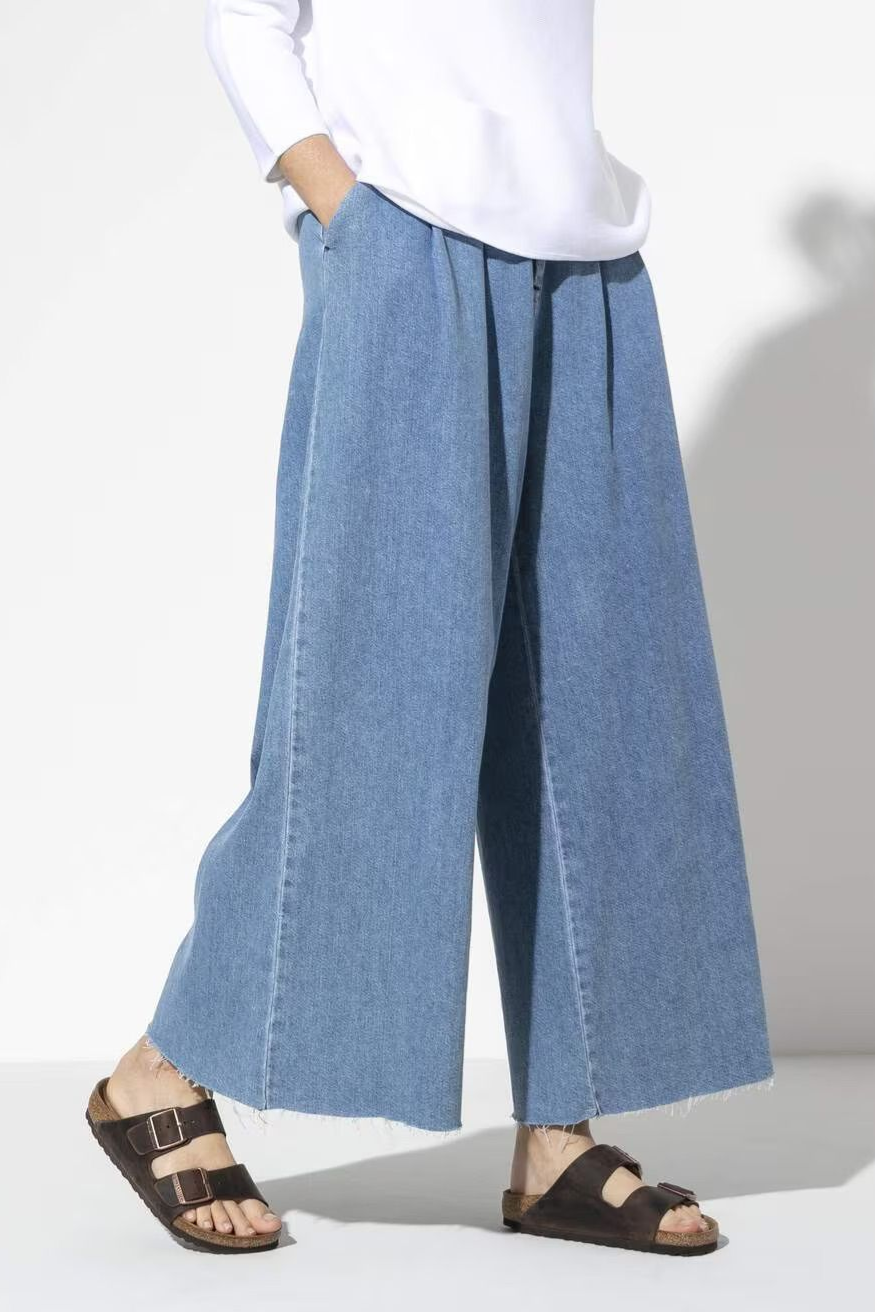 Person wearing wide-leg blue pants and black sandals against a white background