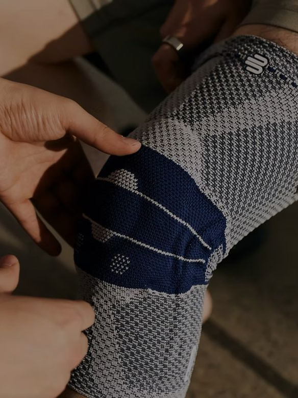 Hands adjusting a gray and navy knee brace on a leg