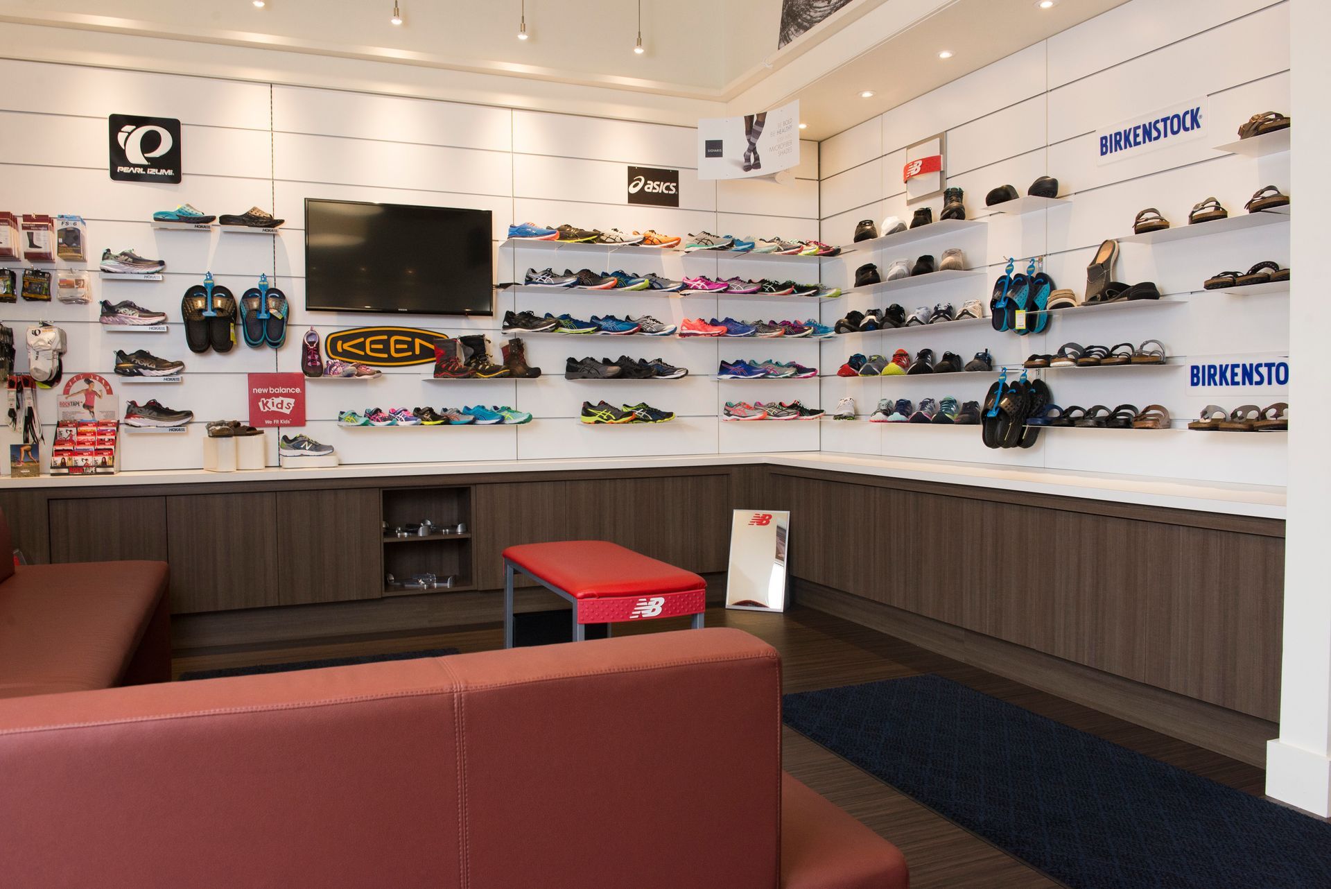 Eyeglass store interior with wall-mounted frames, a TV, and red seating area