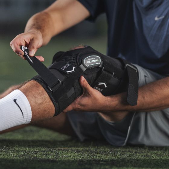 Hands adjusting a gray and navy knee brace on a leg