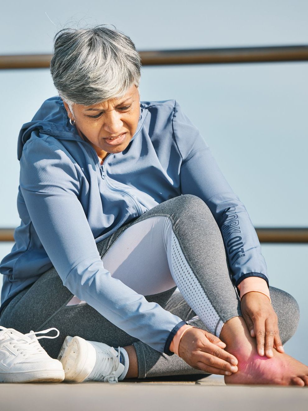 A woman is sitting on the ground holding her ankle in pain.