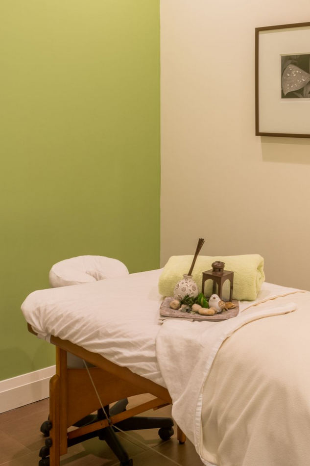 Massage table with white sheets, stones, and candles in a calm room with green and beige walls
