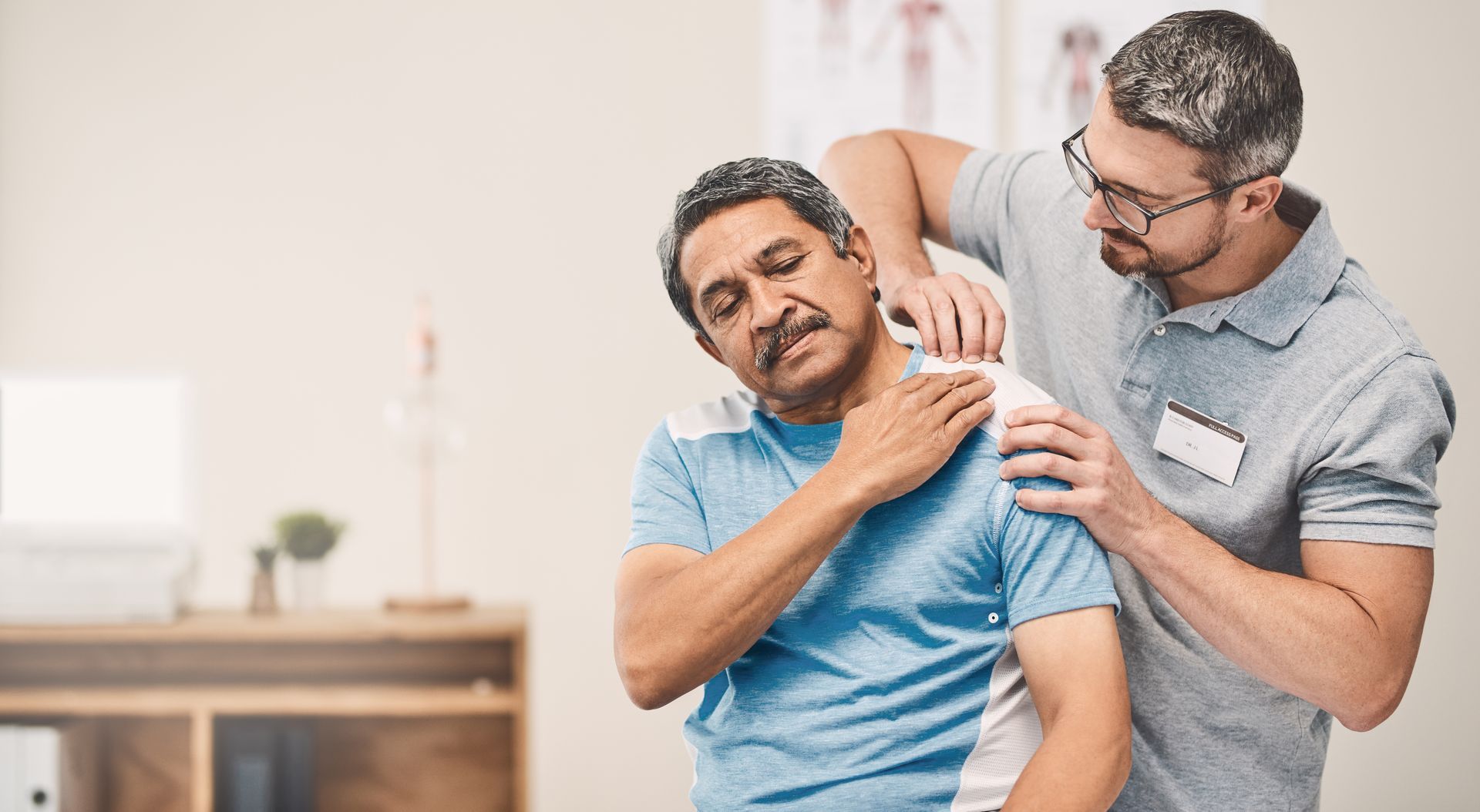 Caregiver helping a man stretch his shoulder in a bright clinic room