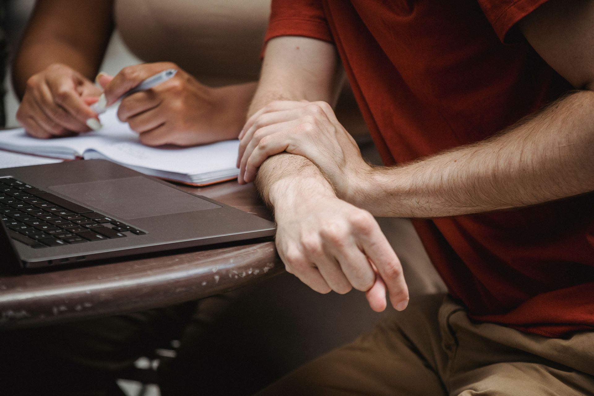 Hands writing on paper beside a laptop on a table