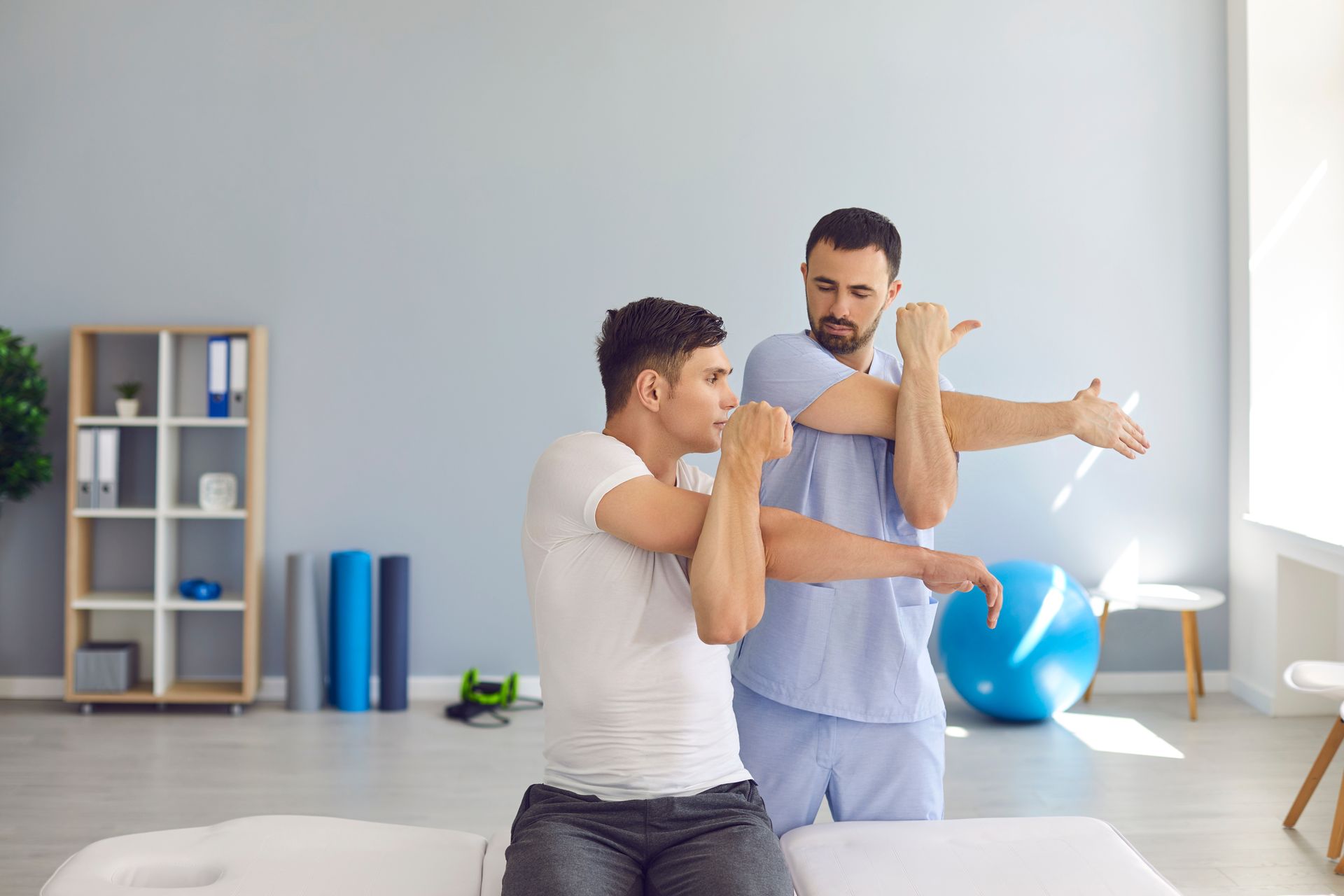 Physical therapist guiding a patient through arm stretches in a bright clinic room