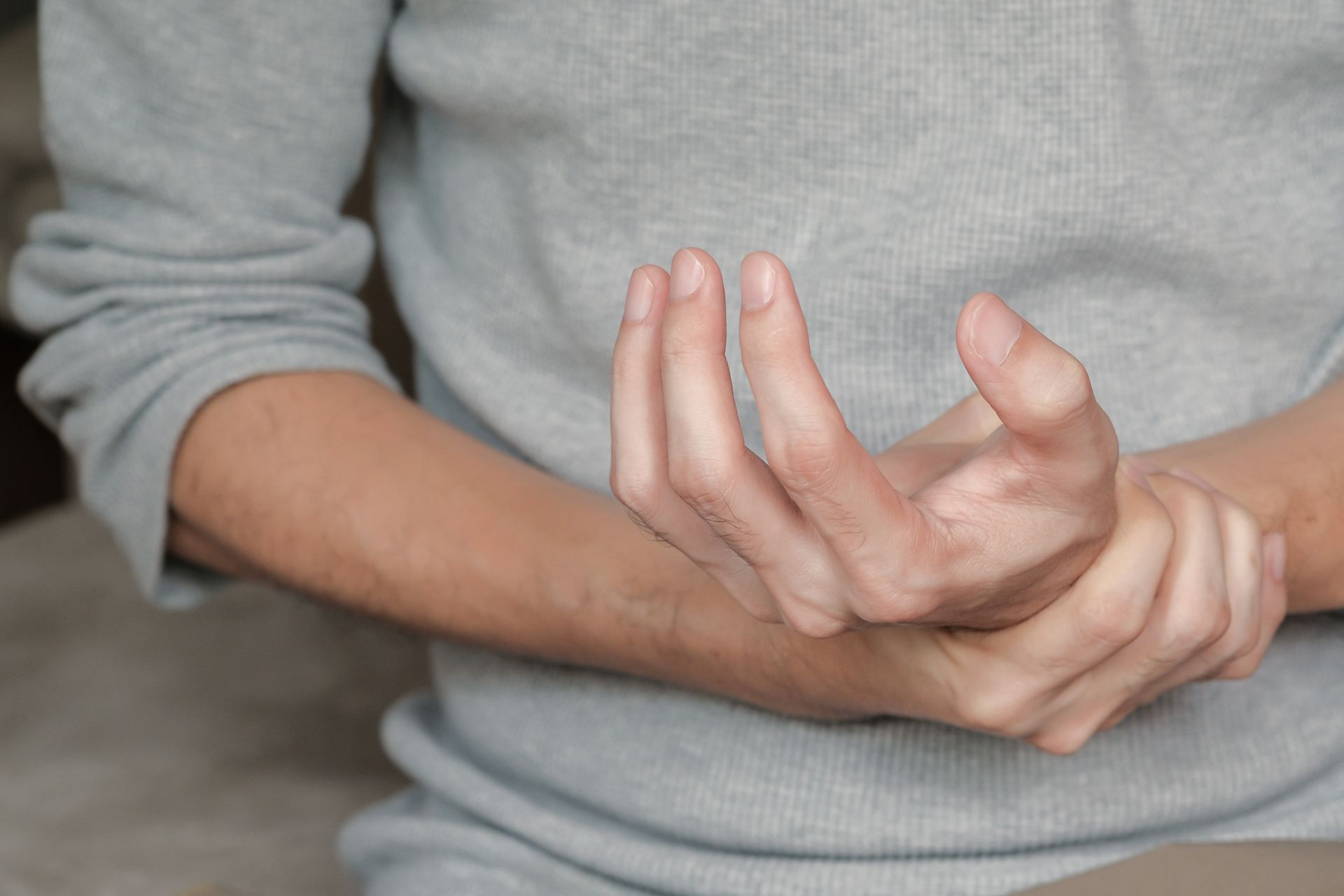 Person holding one wrist and hand, with the other hand bent upward against a gray sweater.