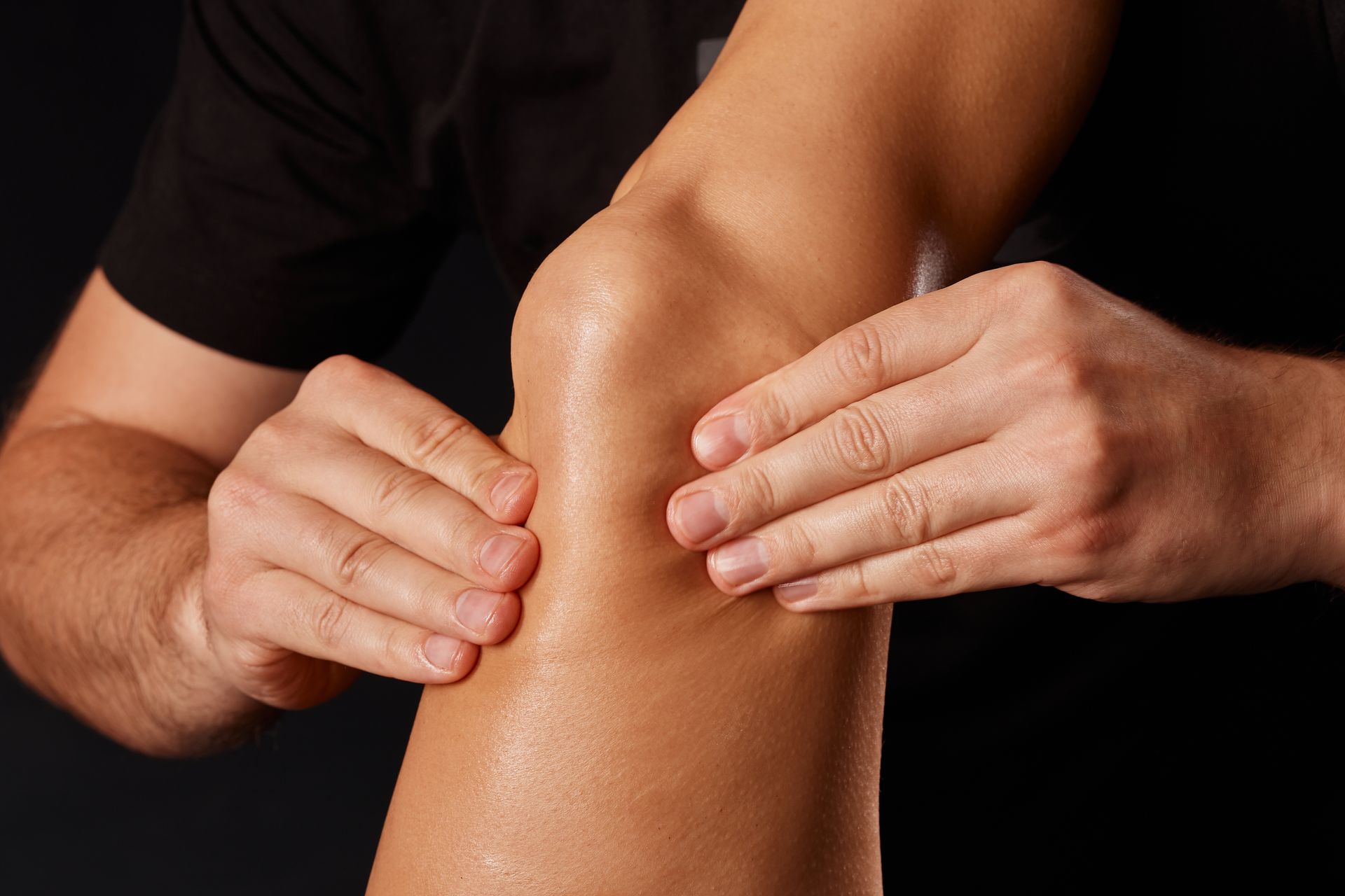 Hands massaging a bent knee on a dark background