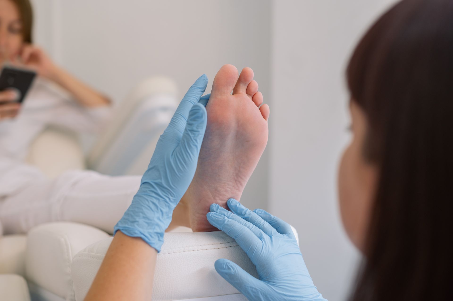 Blue-gloved hands examine a patient’s bare foot during a foot care treatment.