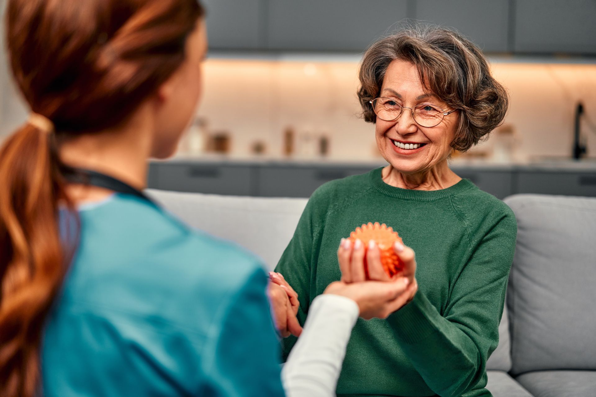Two people smiling and handing over an orange fruit in a kitchen or living room.