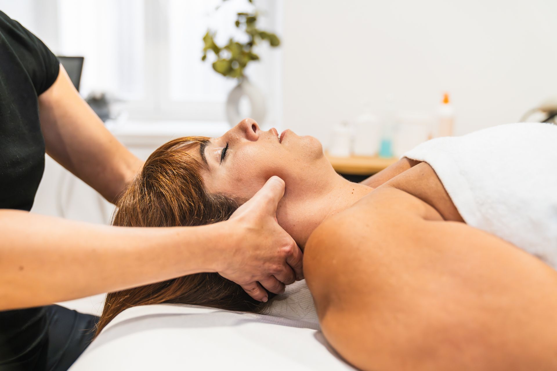 Massage therapist giving a neck massage to a relaxed client on a treatment table