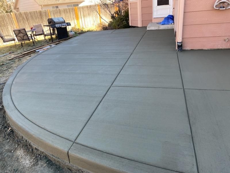 A concrete patio with a grill and chairs in front of a house.