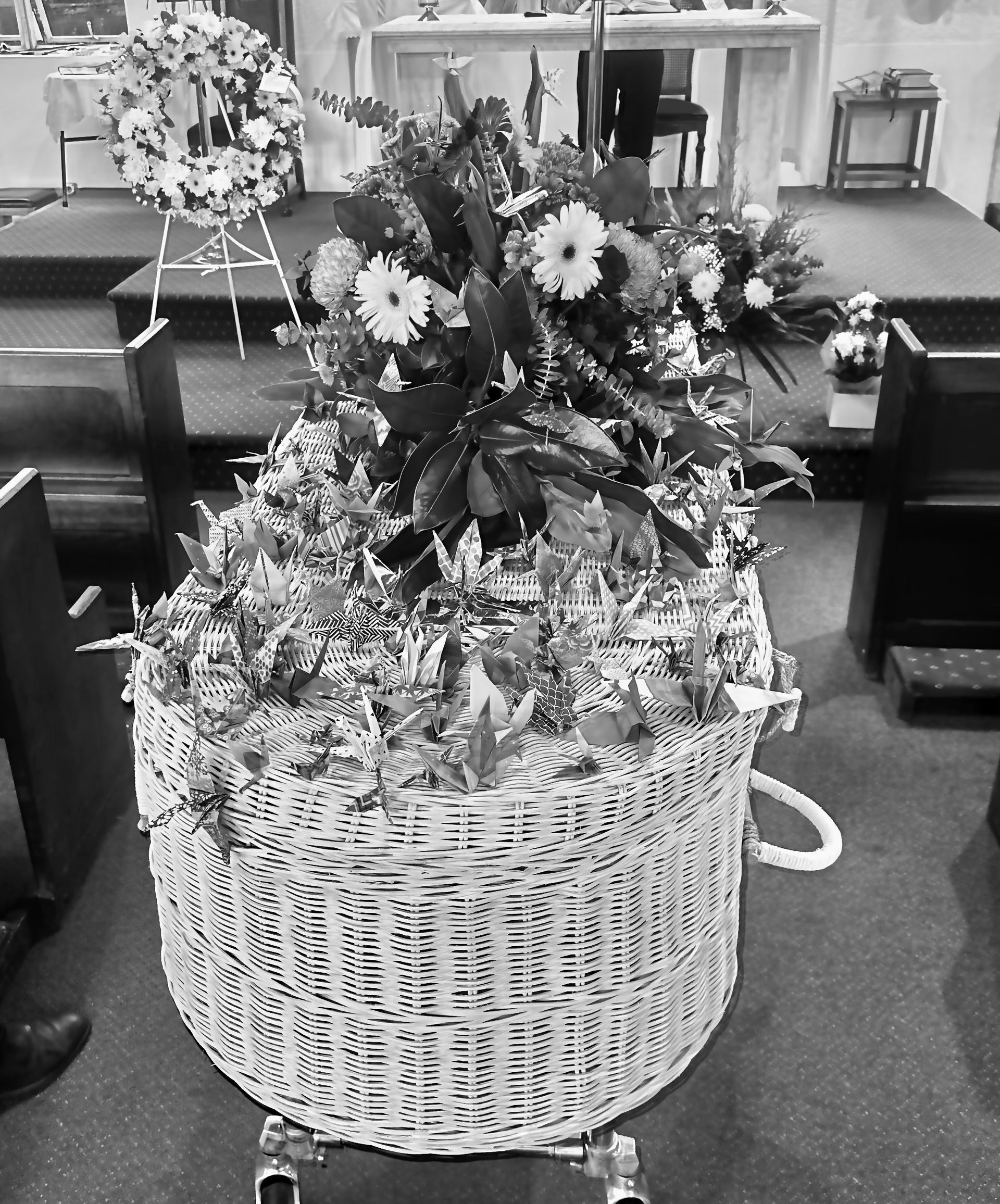 Wicker casket overflowing with flowers, positioned inside a church, likely for a funeral service.