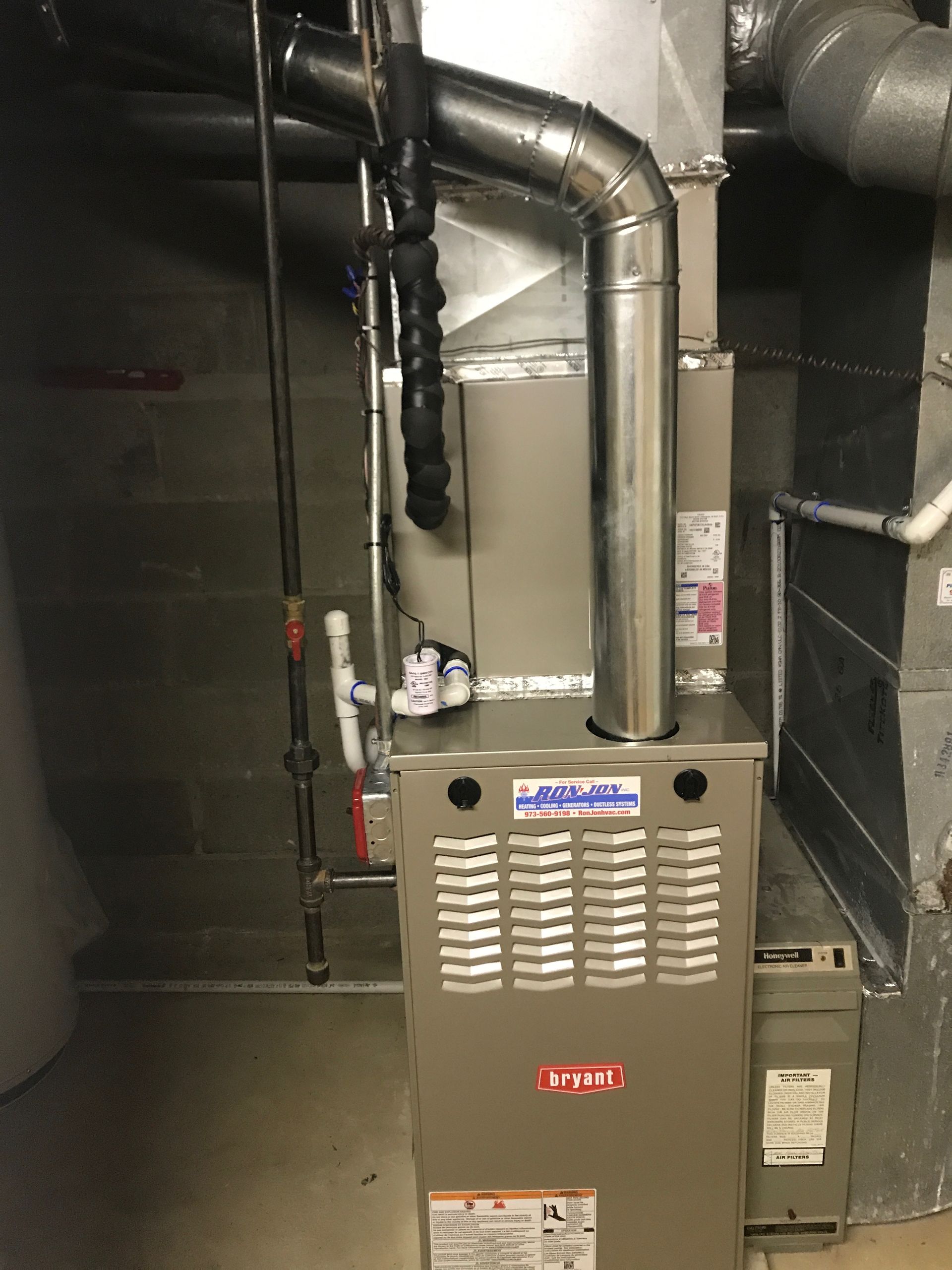 Gas furnace in a utility room with silver ductwork and black pipes.