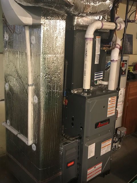Residential HVAC furnace and ductwork in a utility closet, with insulated silver ducts and white PVC pipes.