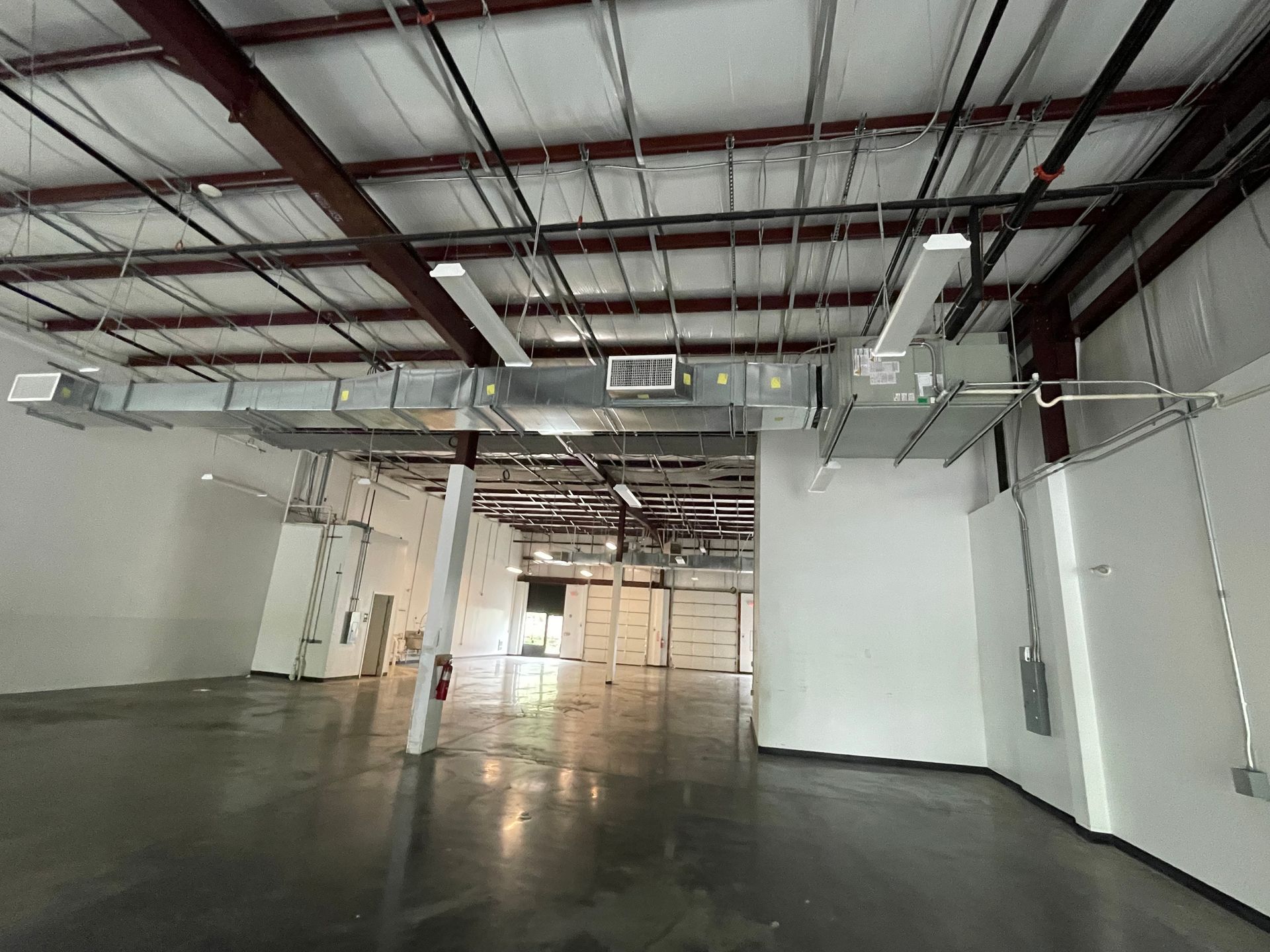 Empty industrial warehouse with white walls, exposed ceiling beams, and a glossy concrete floor