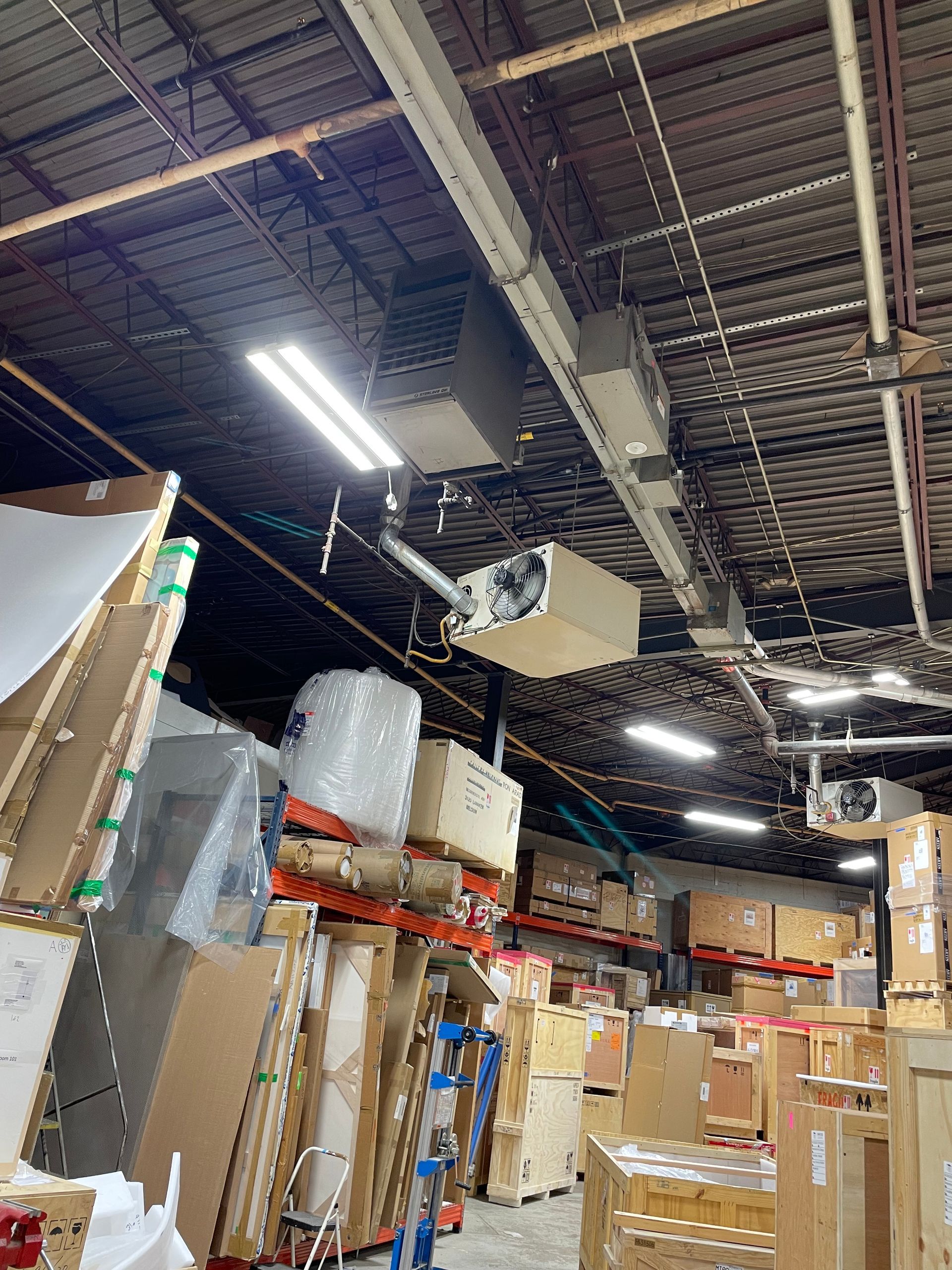 Warehouse storage area with stacked boxes, pallets, and overhead industrial lights under a high ceiling