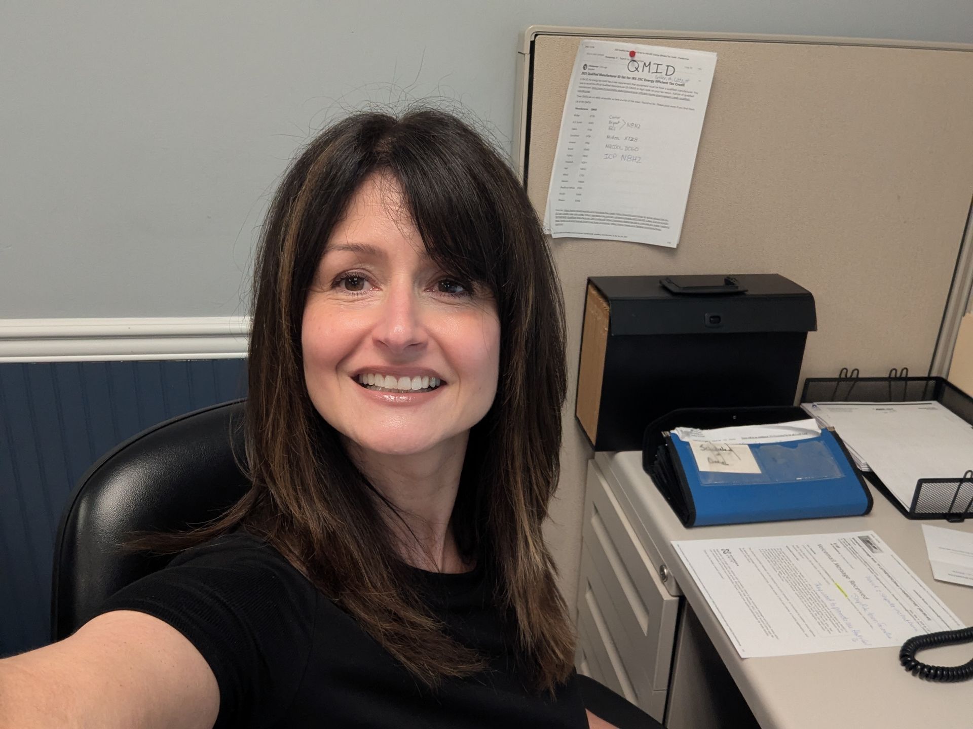 Smiling woman taking a selfie at an office desk with a printer and papers nearby