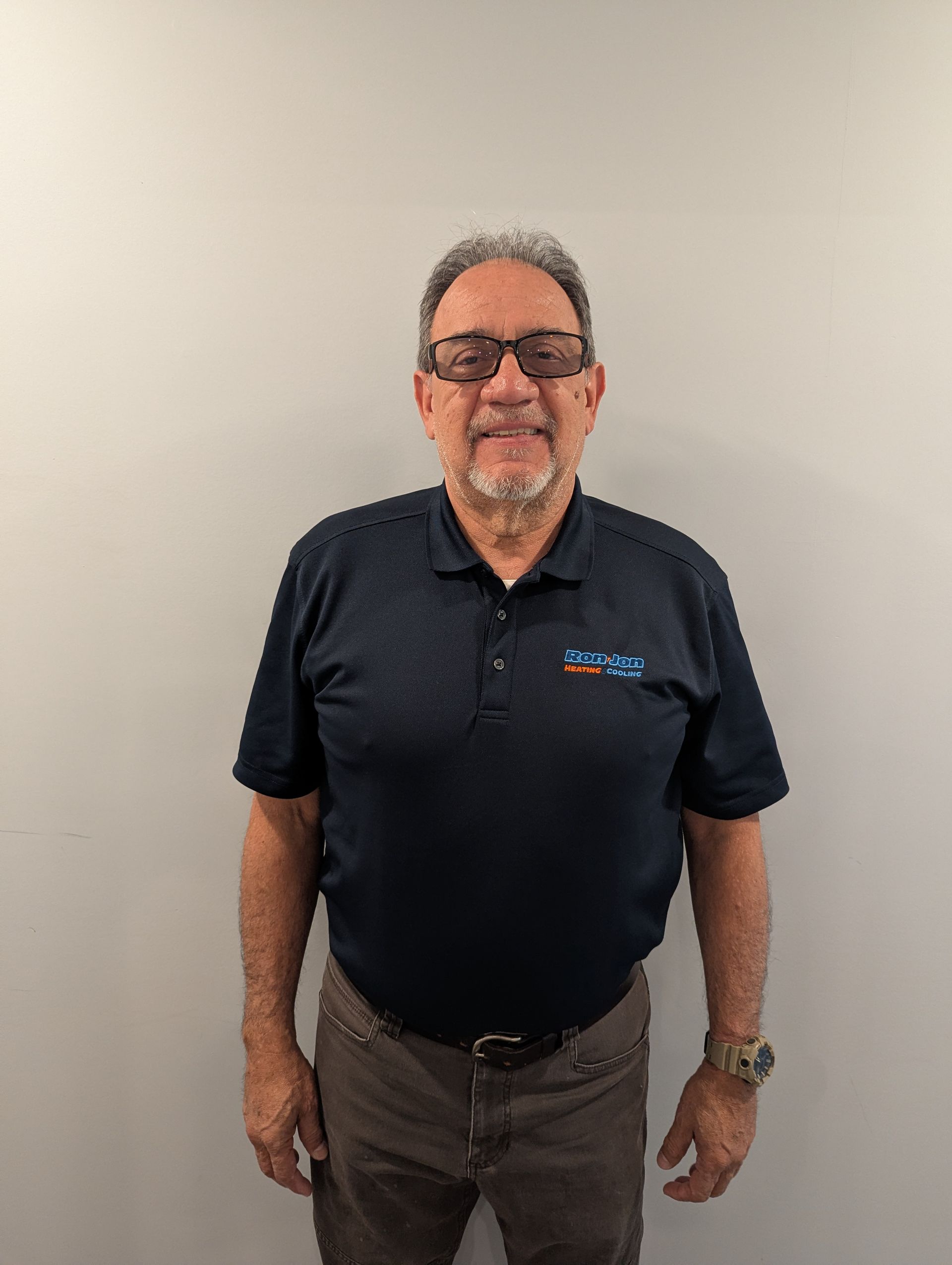 Man standing against a plain wall, wearing a dark polo shirt and glasses.