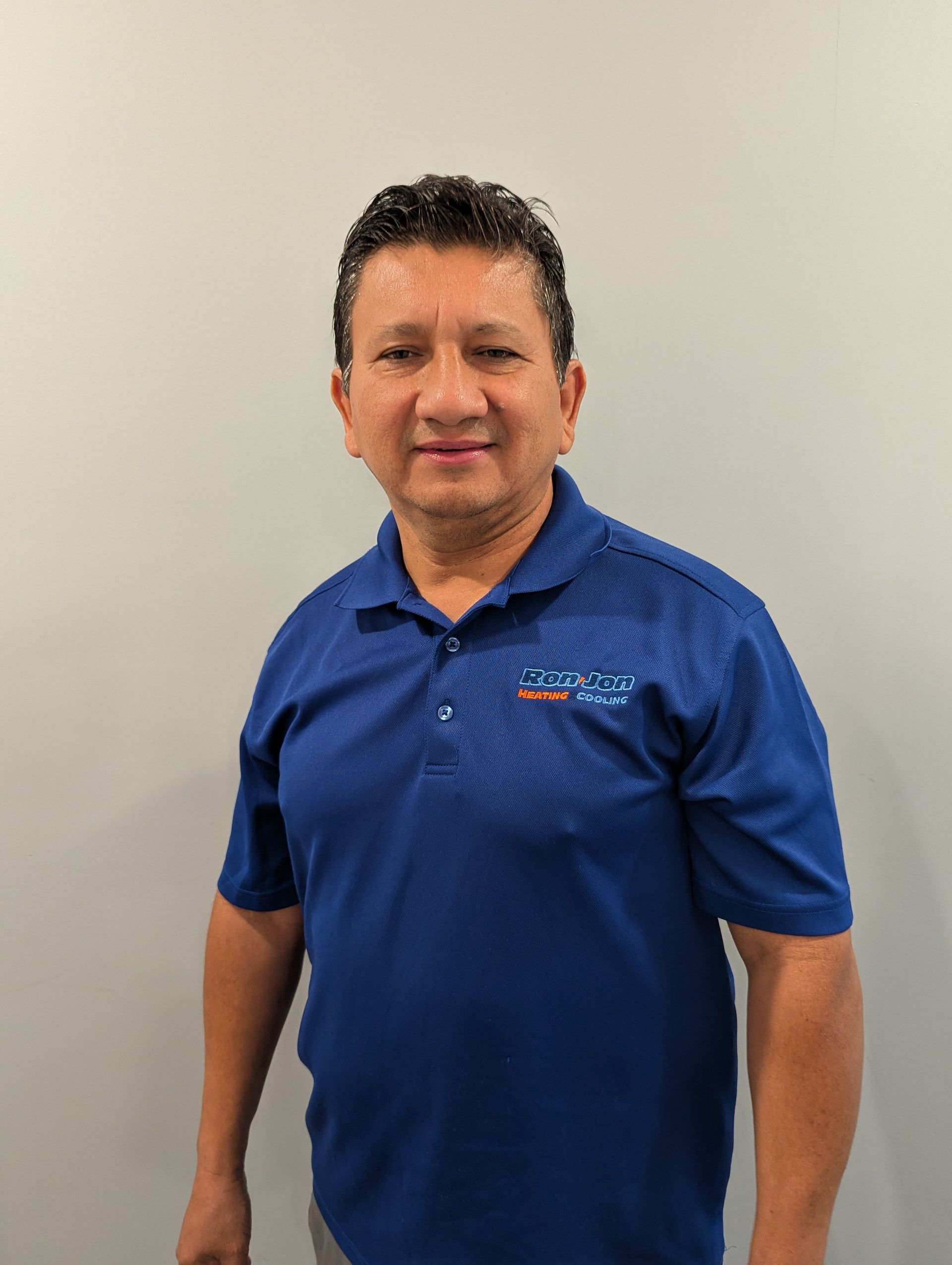 Man in a blue polo shirt standing against a plain wall, facing the camera.