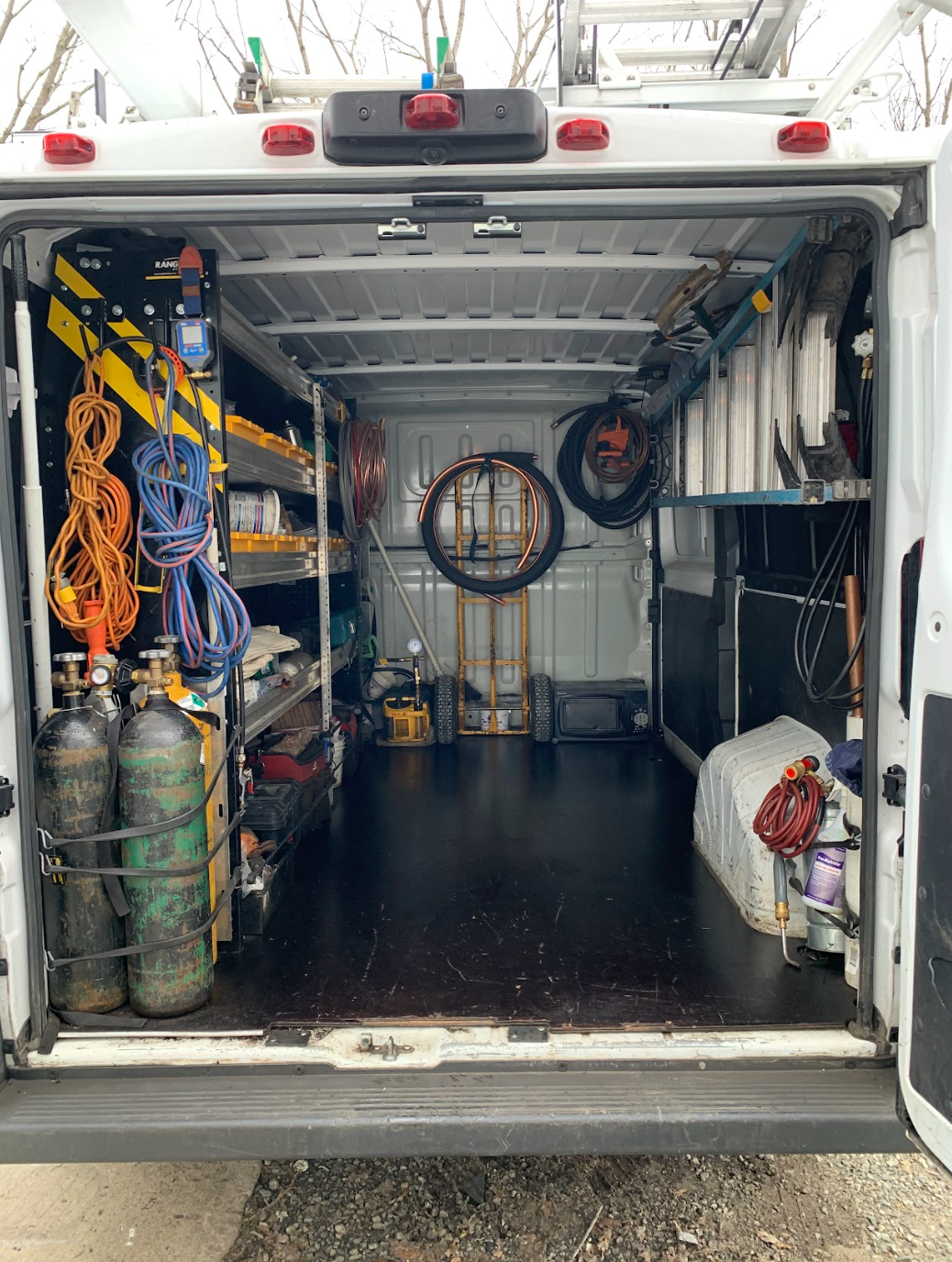 Open utility truck with tools, hoses, tanks, and equipment stored inside the cargo area.