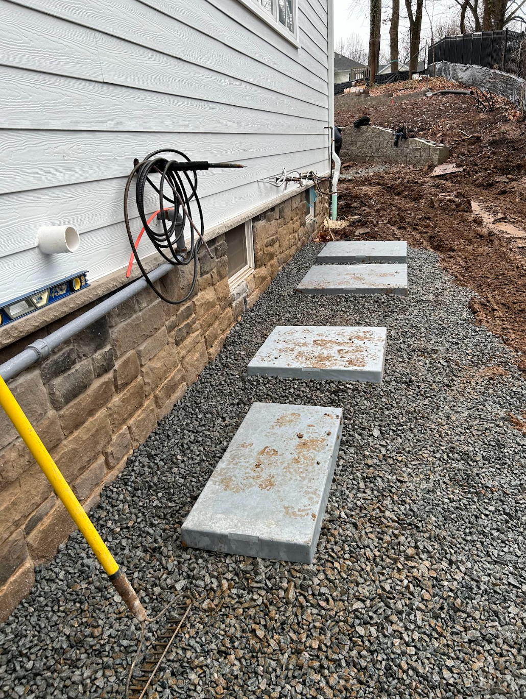 Gravel path with stepping stones beside a house foundation and utility cables along the siding