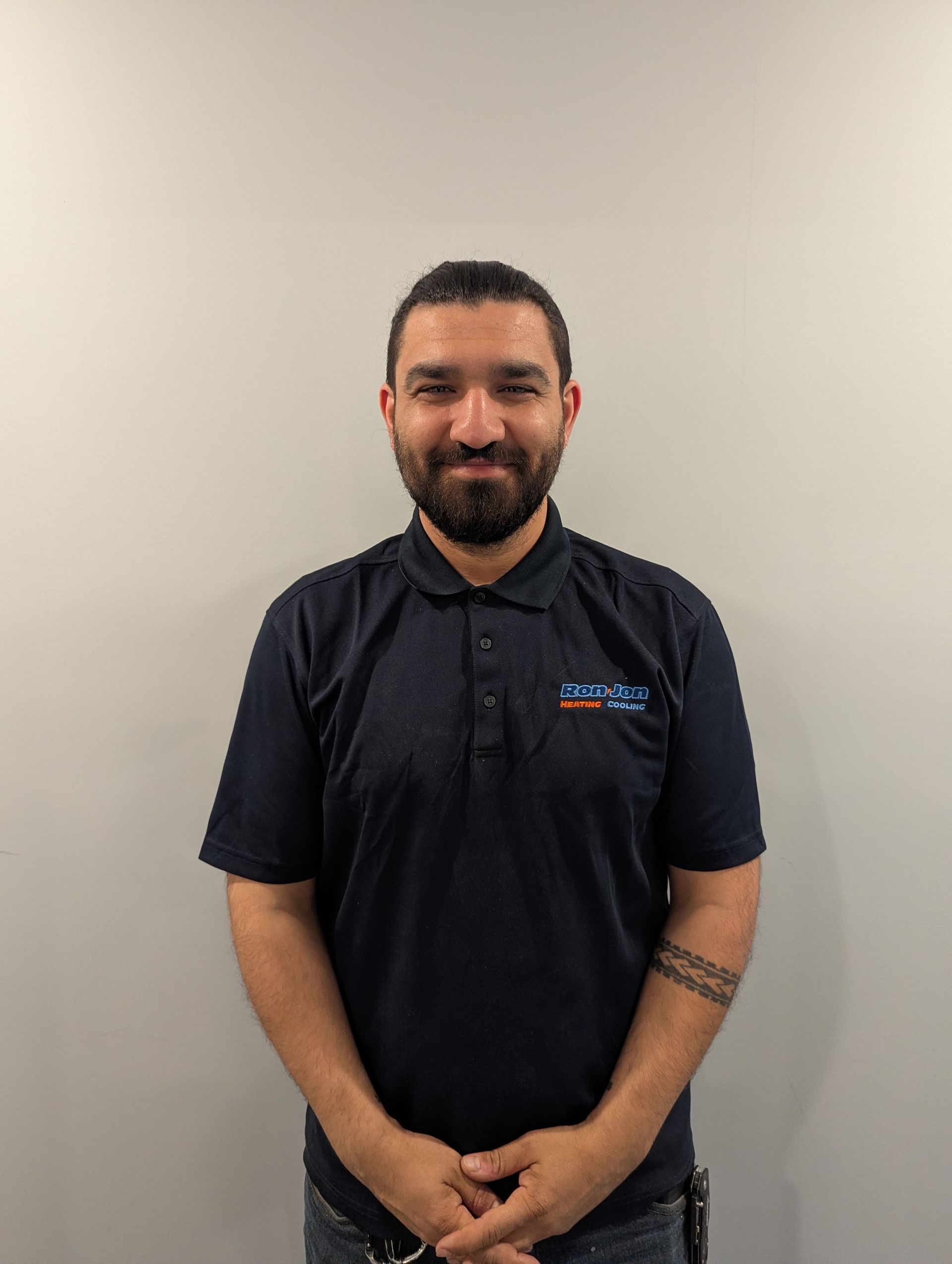 Man standing against a plain wall, wearing a dark polo shirt and smiling gently.