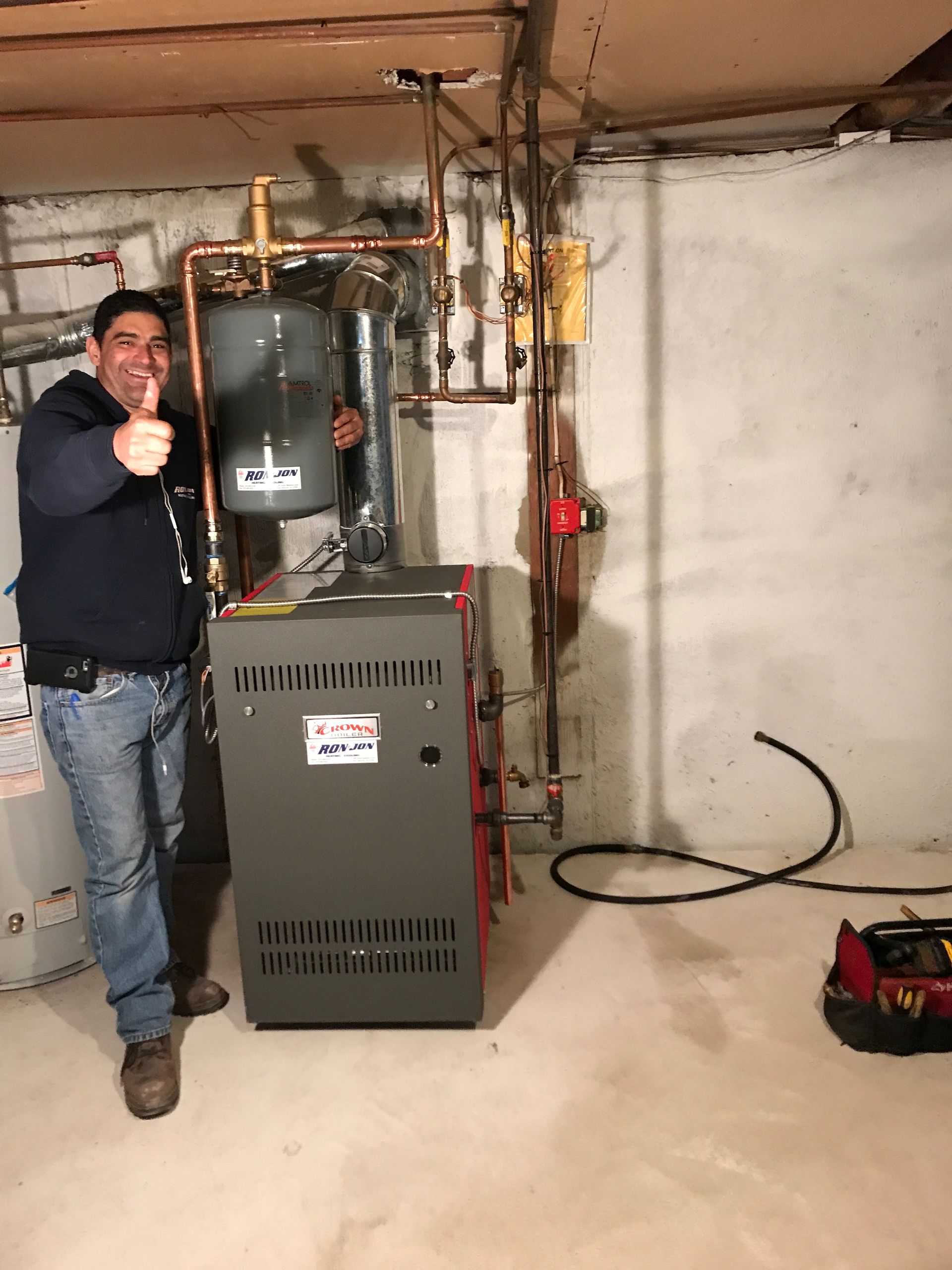 Man standing in a basement beside a furnace and water heater, giving a thumbs-up.