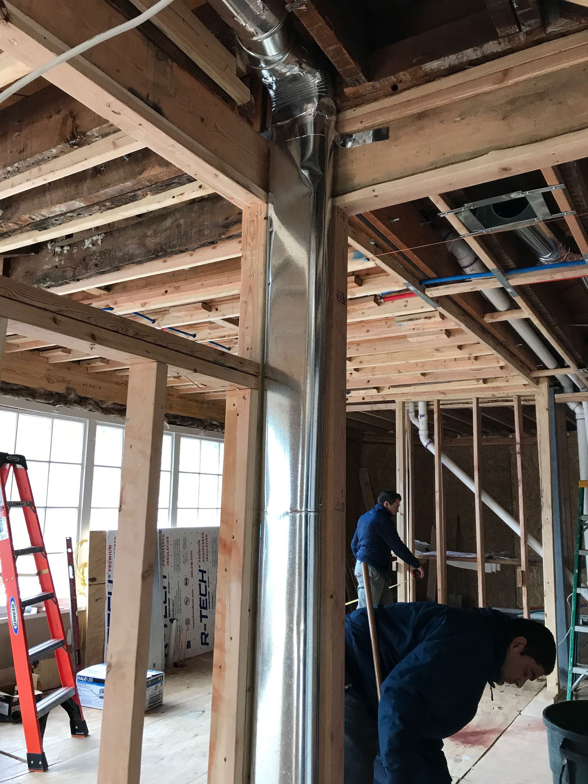 Construction site interior with exposed framing, workers, and a red ladder beside a metal support column