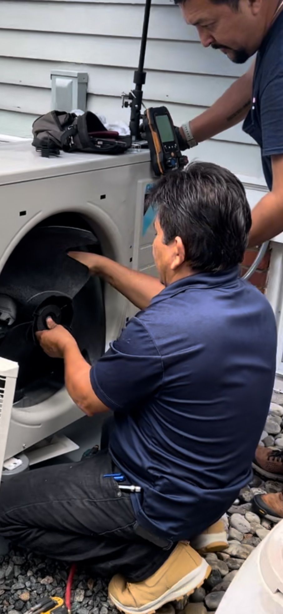 Technicians servicing a front-loading washing machine with tools in a laundry/workshop setting