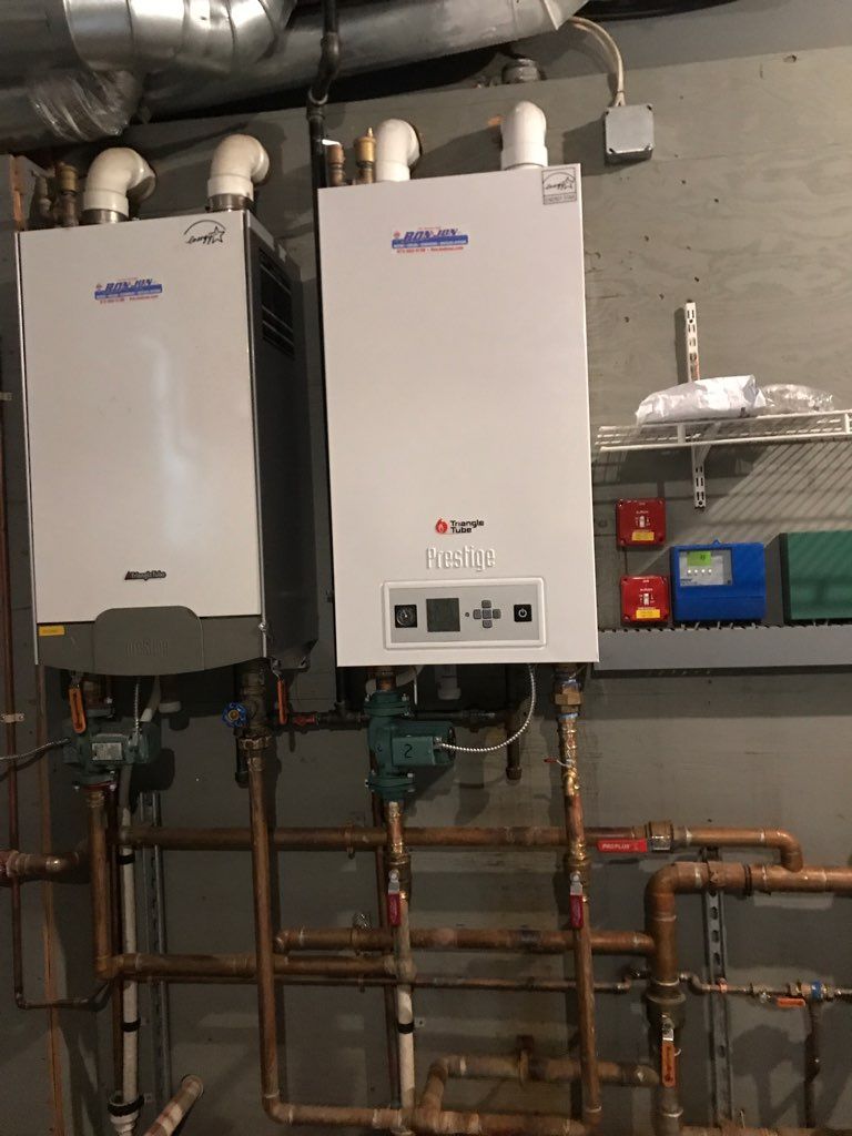 Two wall-mounted white boilers in a utility room with exposed copper pipes and ductwork.