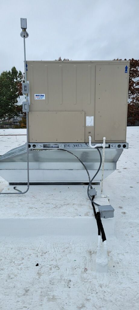 Snow-covered rooftop with beige HVAC unit and rooftop piping, under a cloudy sky