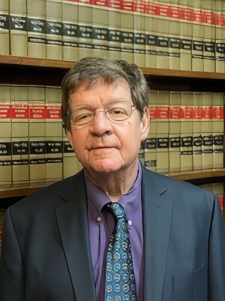 Roy V. Andrews in a suit and tie is standing in front of a bookshelf filled with books.