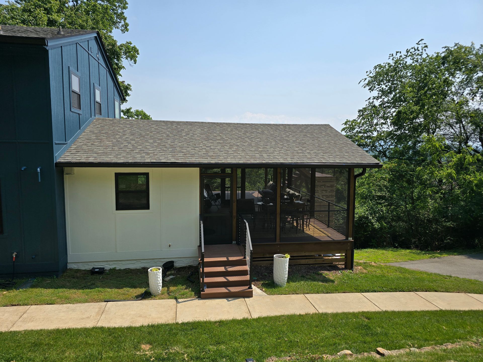 A white building with a screened porch and brown stairs, set on a grassy lawn under a blue sky.