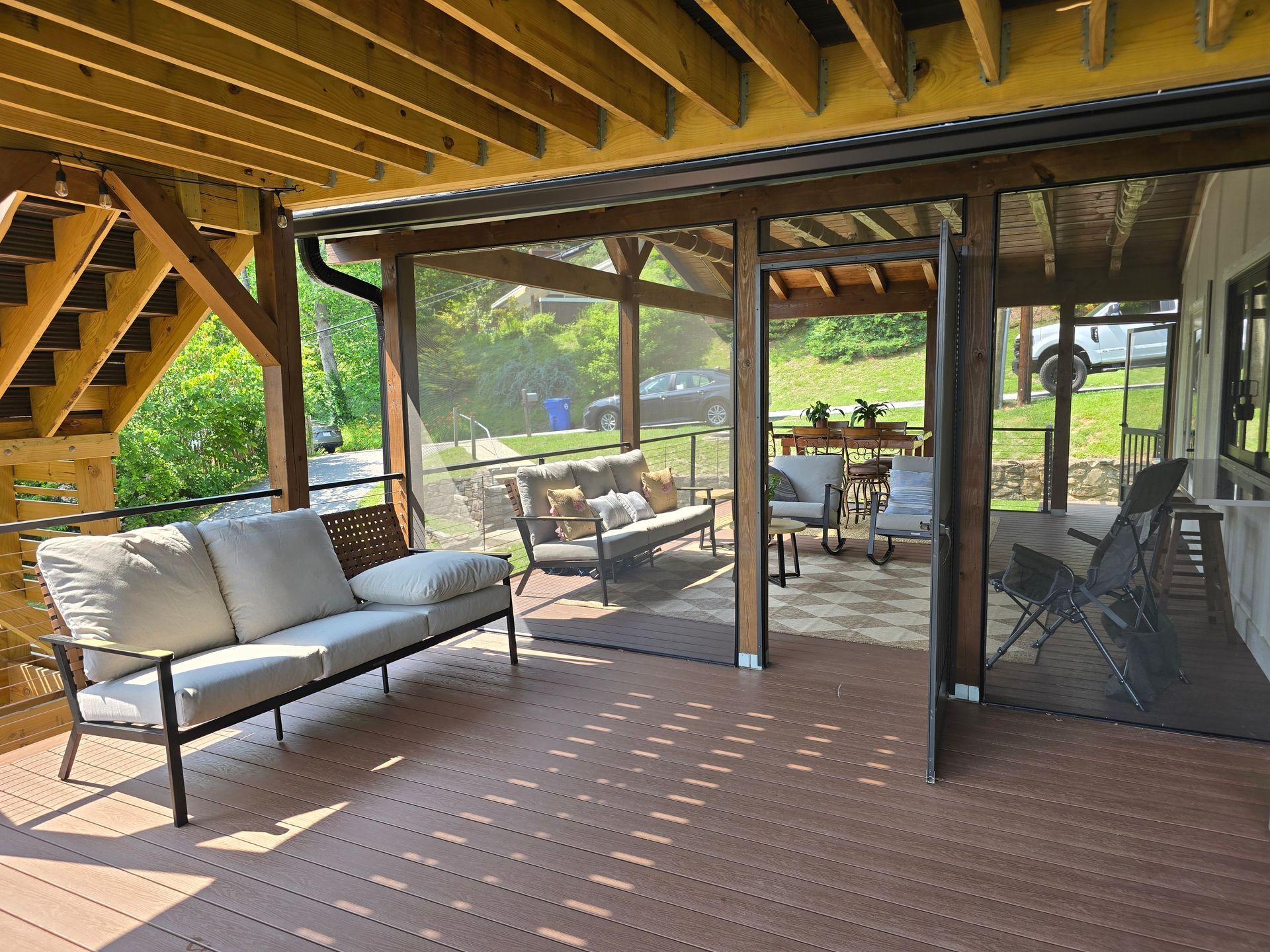 Covered wooden deck with outdoor furniture, screening, and stairs.