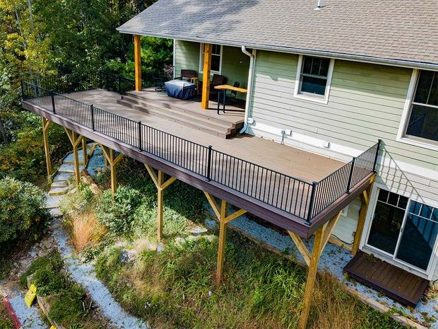 Elevated wooden deck attached to a house with black railing. Supports are visible.