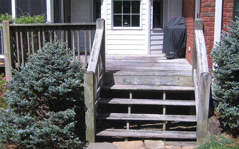 Wooden steps leading to a weathered deck and white door with a covered grill.