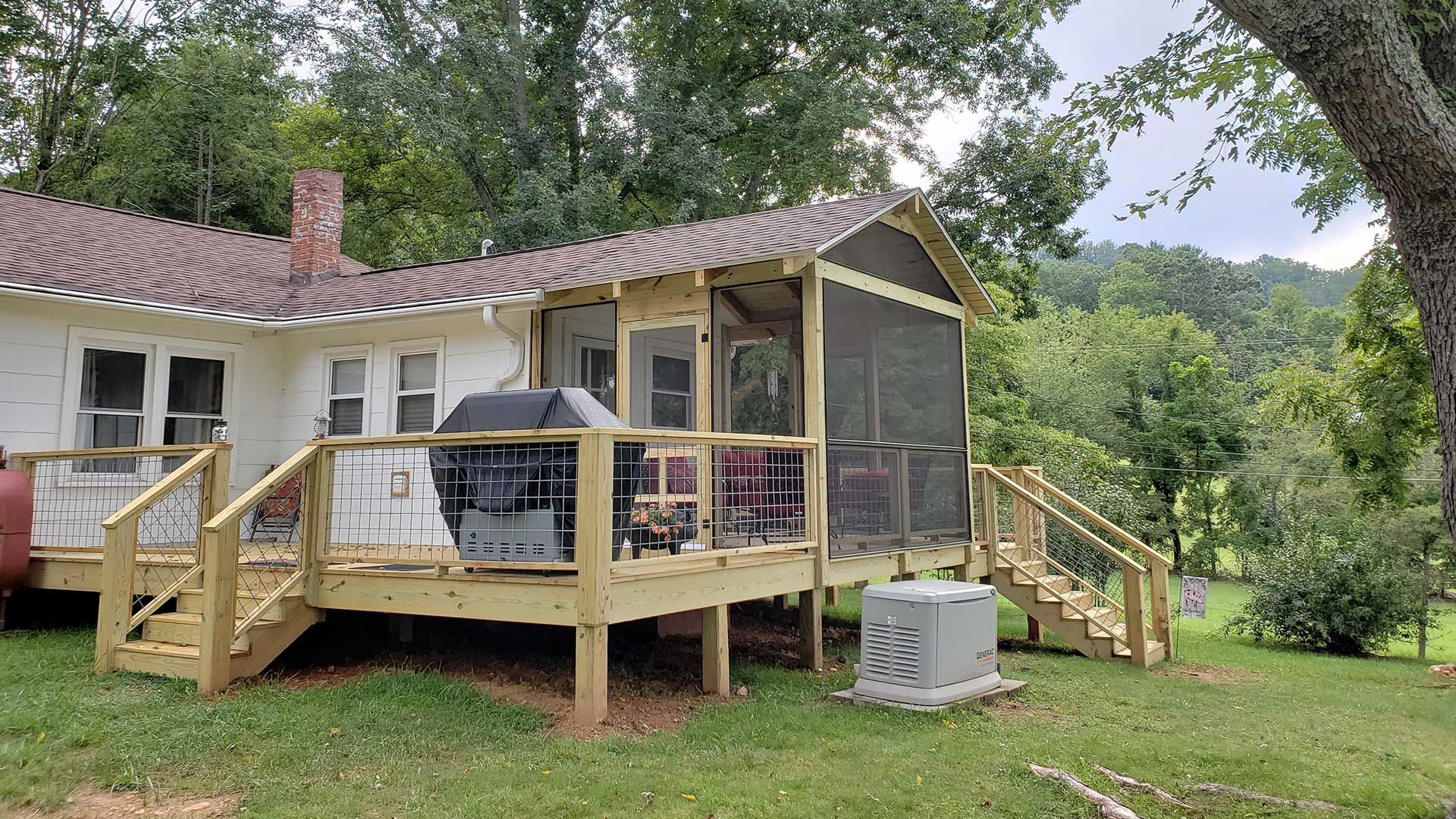 Wooden deck with screen porch attached to a white house, grill on deck, steps leading down to grassy yard.