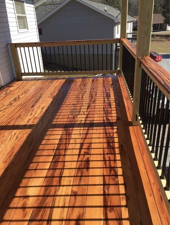 Wooden deck with black metal railing, sunlight casting shadows.