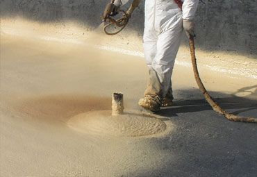 Person in protective suit spraying foam insulation onto a surface.