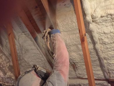 Person spraying insulation into an attic. Wooden beams and expanding foam are visible.